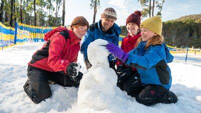 Mum, Dad, Daghter, and Son kneeling around a snowman which they are putting sunglasses on.